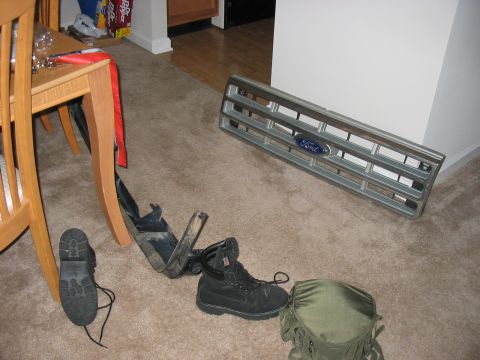 1988 Ford Bronco - A Ford grille and work boots are laid out on a carpeted floor, possibly for repair or replacement.