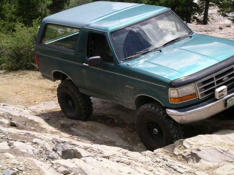 1996 Ford Bronco - A green Ford Bronco navigates a rocky trail, its off-road capabilities.