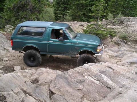 1996 Ford Bronco - A green Ford Bronco navigates a rocky trail, its off-road capabilities.