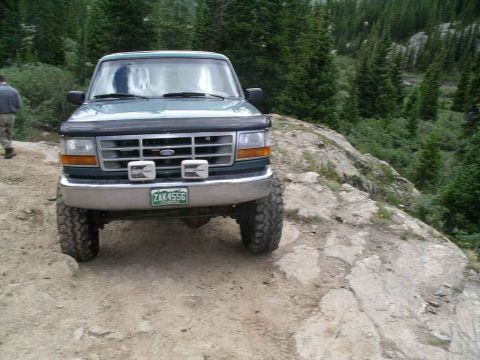 1996 Ford Bronco - A green 1996 Ford Bronco navigates a mountain path, its off-road capabilities.