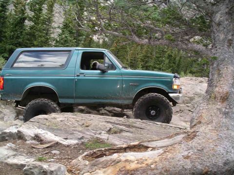 1996 Ford Bronco - A green Ford Bronco navigates a rocky trail in a wooded area.