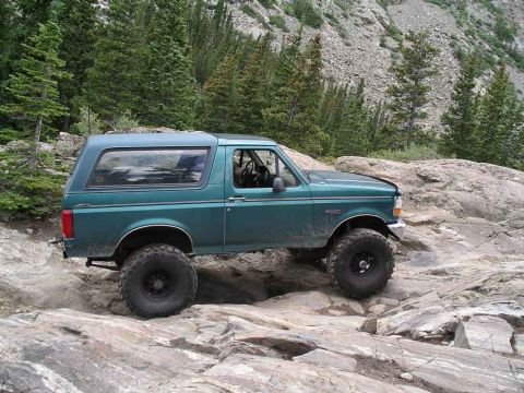 1996 Ford Bronco - A green Ford Bronco tackles a challenging rocky path in a mountainous area.