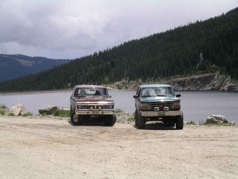1996 Ford Bronco - Two Ford Broncos parked by a lake with a mountain backdrop.