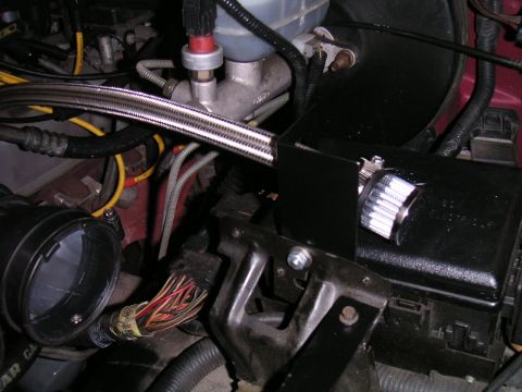 1994 Ford Bronco - Engine bay detail showing a braided stainless-steel line routed past the brake master cylinder and translucent reservoir, with a chrome-mes…