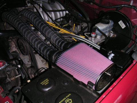 1994 Ford Bronco - Engine bay detail of a red vehicle showing a large pink conical K&N-style cone air filter clamped to a black intake tube, with a corrugated…