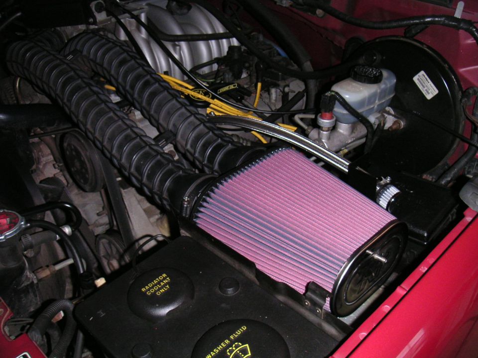 Pink cone air filter and intake tube in a red truck's engine bay with yellow plug wires