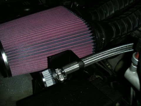 1994 Ford Bronco - Close-up of a red oiled-gauze conical cone air filter mounted on a black intake tube inside an engine bay, with a black bracket and stainle…