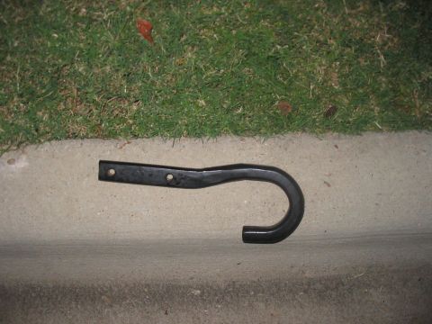 1988 Ford Bronco - A single tow hook is shown lying on a concrete curb next to grass.