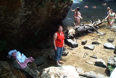 1985 Ford LTD Crown Victoria - A group of people enjoy a day at a rocky river, with some swimming and others standing near the shore.