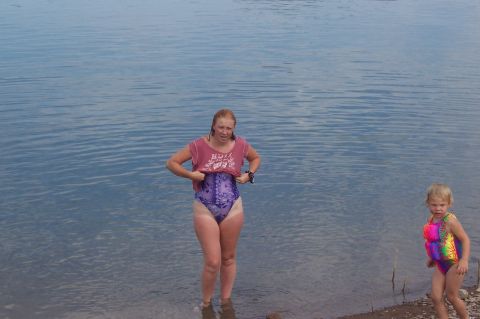 1992 Ford Bronco - A woman adjusts her swimsuit while a child stands nearby at the edge of a body of water.