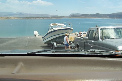 1992 Ford Bronco - A truck is backing a boat on a trailer down a ramp towards a large body of water.