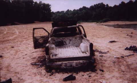 1989 Ford Bronco - This heavily damaged pickup truck appears abandoned in a sandy, outdoor environment, with its doors ajar.