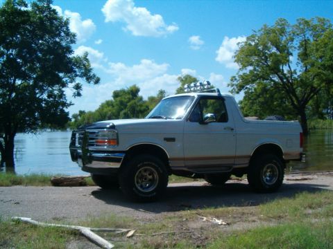 1996 Ford Bronco - A white 1996 Ford Bronco is parked near a body of water under a blue sky with clouds.