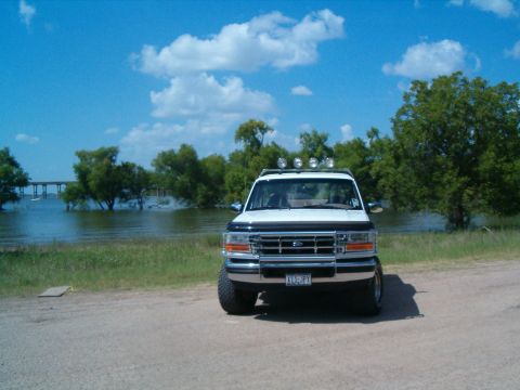 1996 Ford Bronco - 1996 Ford Bronco parked by the water under a blue sky with clouds.
