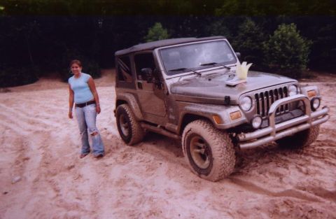 1989 Ford Bronco - A woman stands next to a brown Jeep Wrangler on a sandy terrain.