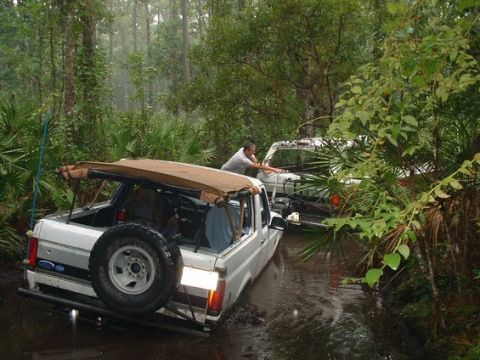 1992 Ford Bronco - Two Ford Broncos navigate a muddy, wooded trail on a rainy day.