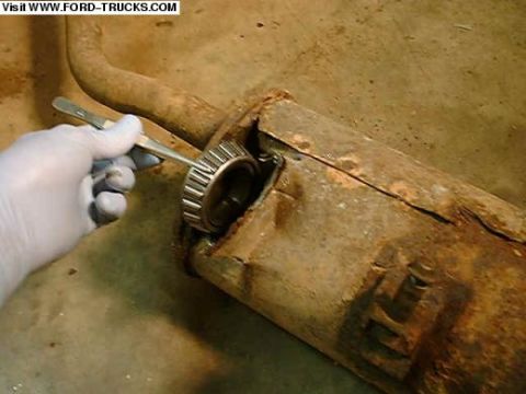 1996 Ford Bronco - A gloved hand uses a tool to remove a bearing from a heavily rusted exhaust pipe.