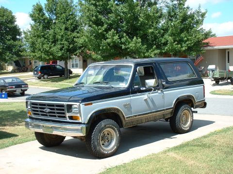 1982 Ford Bronco - A two-tone black and silver Ford Bronco is parked on a driveway, with other vehicles visible in the background.