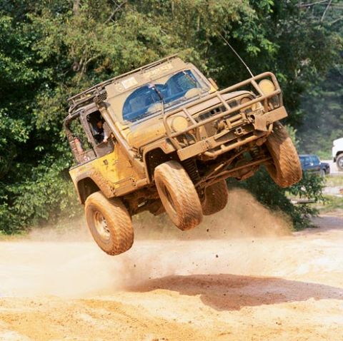 1990 Ford Bronco - This off-road vehicle is captured mid-air during an off-road event, kicking up dust.