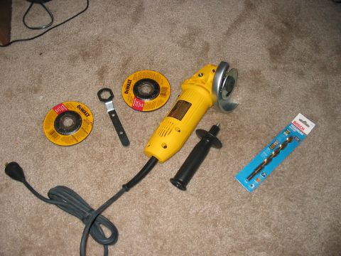1988 Ford Bronco - Tools laid out on a carpeted floor, including an angle grinder, cutting discs, and a drill bit.