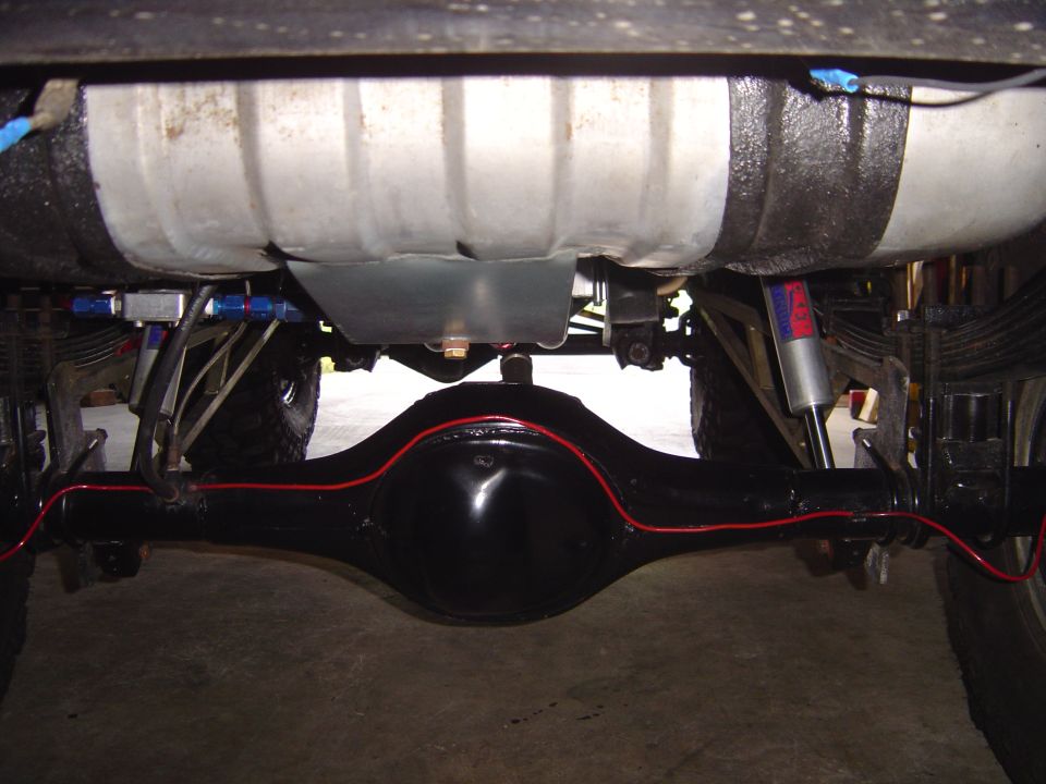 Underside of a vehicle showing a large fuel tank, rear axle, leaf springs, and shocks