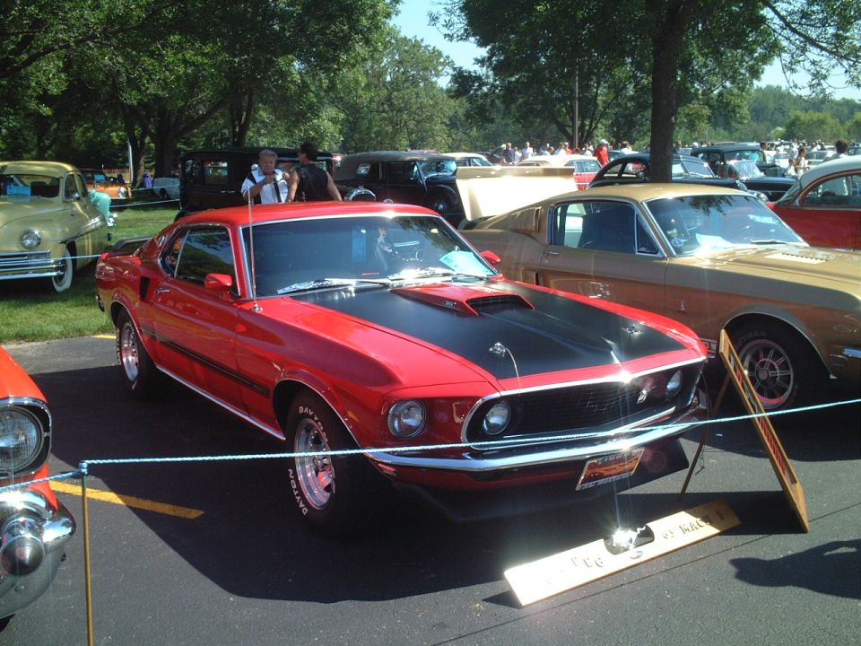 Red 1969 Mustang Mach 1 fastback with black hood on display at a car show