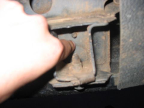 1988 Ford Bronco - A close-up shows a rusty bracket on a vehicle's frame, with a finger indicating a bolt.