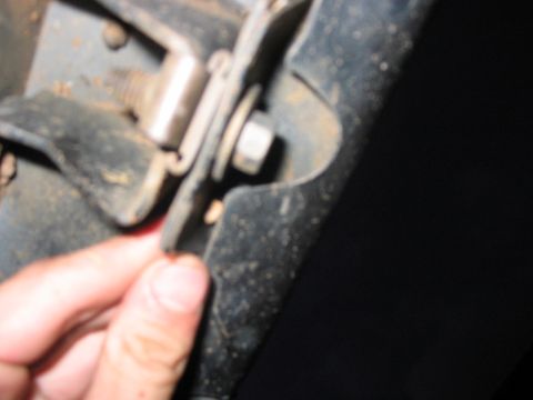 1988 Ford Bronco - A hand inspects a rusty metal bracket with a bolt and nut attached to a vehicle's frame.