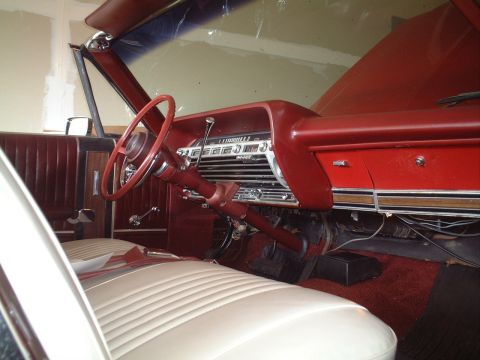 1967 Ford Galaxie - The interior of a 1967 Ford Galaxie shows a red dashboard, steering wheel, and door panels with white seats.