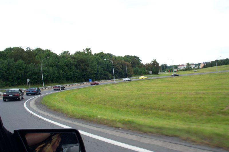 Convoy of cars curving along a highway ramp seen from a moving car's window, mirror in corner