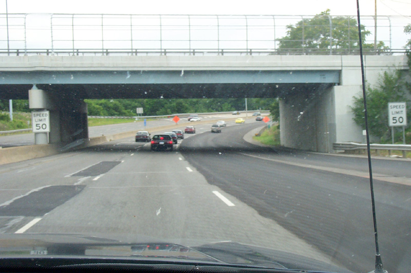 Windshield view approaching highway overpass with Speed Limit 50 signs