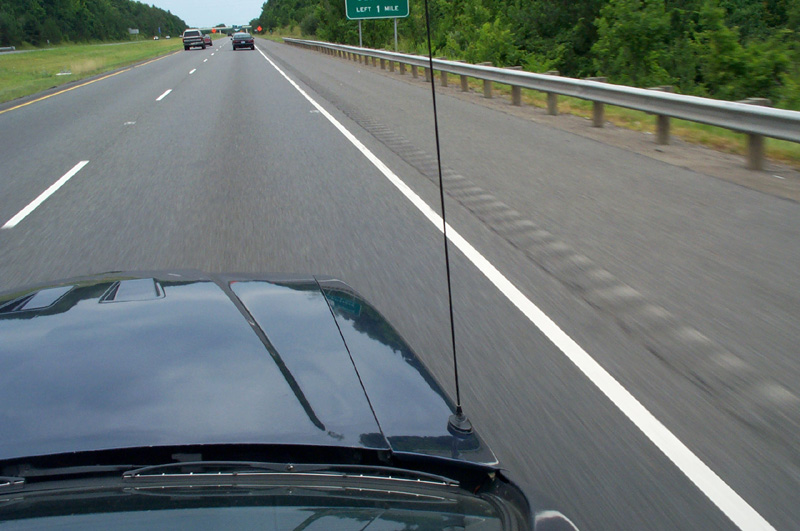 View over dark blue sedan trunk and whip antenna while driving on a highway
