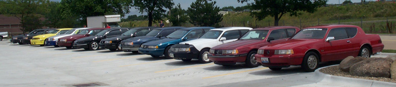 Row of a dozen Thunderbird and Cougar coupes parked nose-out at a lot meet, red cars nearest