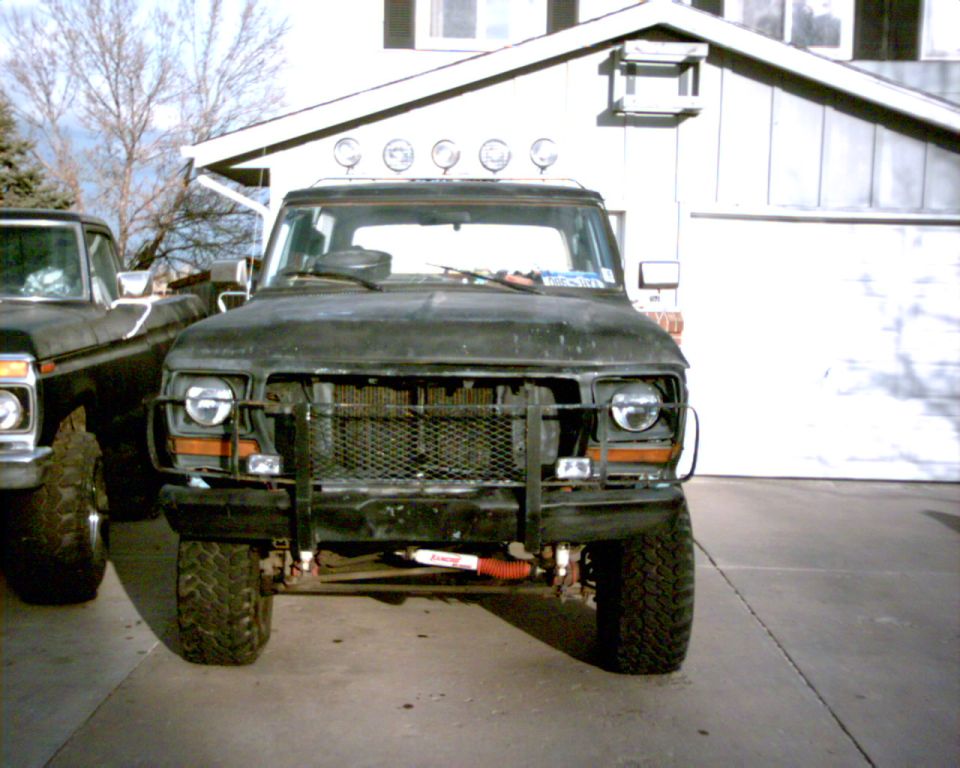 Lifted dark Ford truck with brush guard and light bar parked by a garage