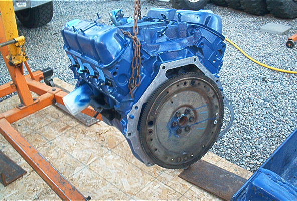 Blue engine block suspended by a chain on an orange engine hoist