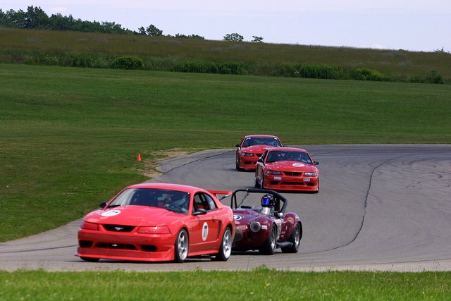 Red Mustangs and a roadster racing on a road course track