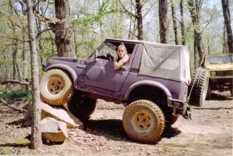 1978 Ford Bronco - A woman drives a purple Suzuki Samurai over rocks on a wooded trail, with another Suzuki Samurai visible behind it.