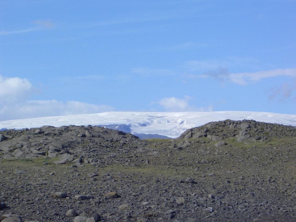 Rocky terrain with distant snow-covered glacier under blue sky