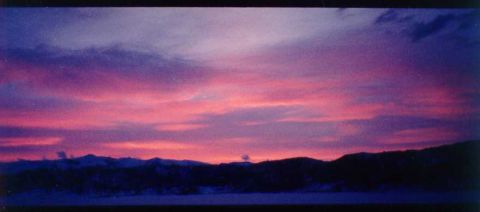 1996 Ford Bronco - A vibrant sunset paints the sky with hues of purple and pink above a silhouetted mountain range.