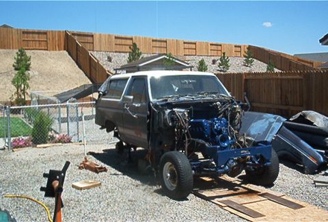 1986 Ford Bronco - Disassembled Ford Bronco with exposed engine and front end, parked outdoors on a gravel surface.