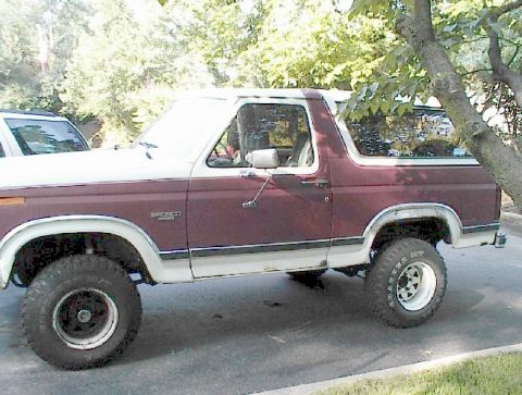 1984 Ford Bronco - Side view of a maroon and white 1984 Ford Bronco, parked outdoors.