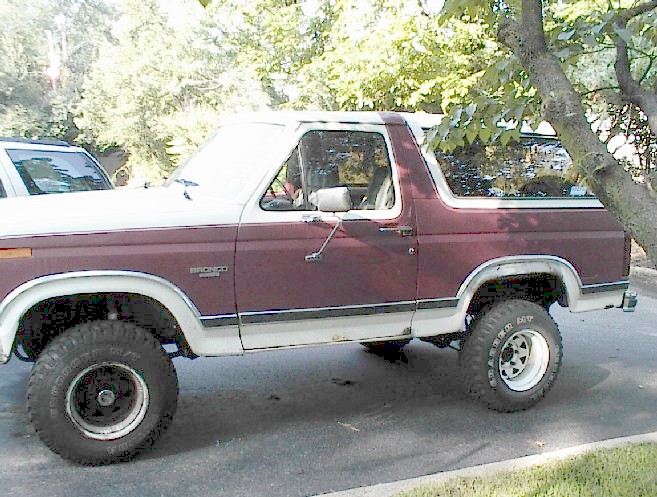 Maroon and white 1984 Ford Bronco parked next to a white SUV