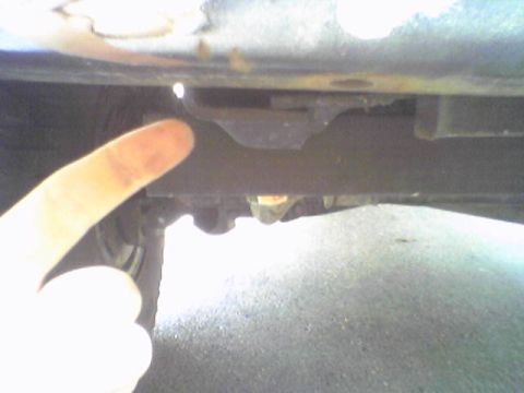 1993 Ford Bronco - A finger points to a metal bracket on the undercarriage of a vehicle.