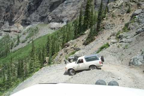 1990 Ford Bronco - A white SUV navigates a challenging off-road trail on a steep mountainside.