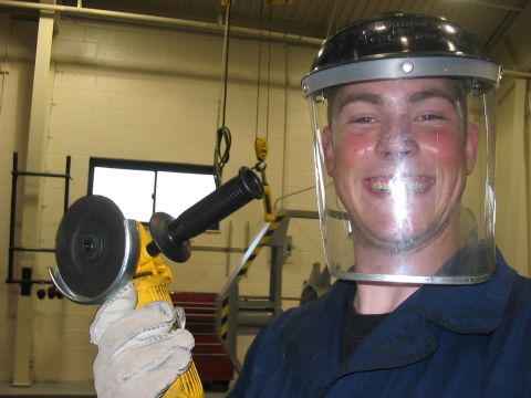 1988 Ford Bronco - Man wearing a face shield and holding an angle grinder in a workshop setting.