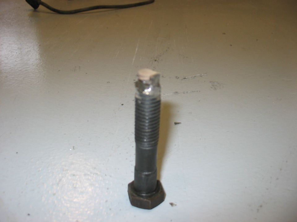 Bolt with a nut on a light gray surface. Supermotors logo at bottom right