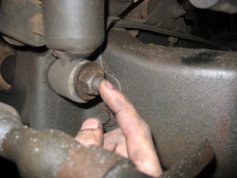 1988 Ford Bronco - A finger points to a sway bar link bolt and bushing, likely from a vehicle's suspension system.