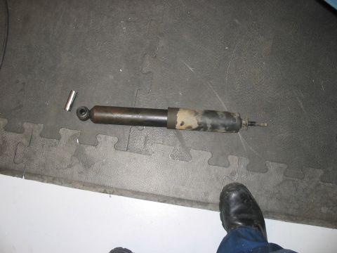 1988 Ford Bronco - A single shock absorber lies on a black mat next to a small metal cylinder and rubber bushing.