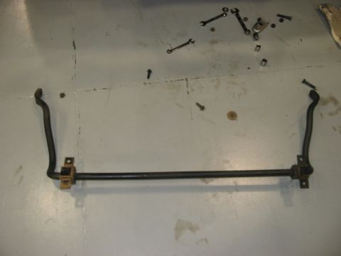 1988 Ford Bronco - A sway bar lies on a garage floor next to various tools and hardware.