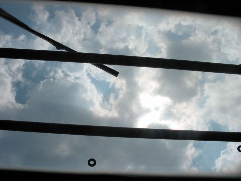 1988 Ford Bronco - The view through a vehicle's windshield shows wipers against a sky filled with clouds and sunlight.